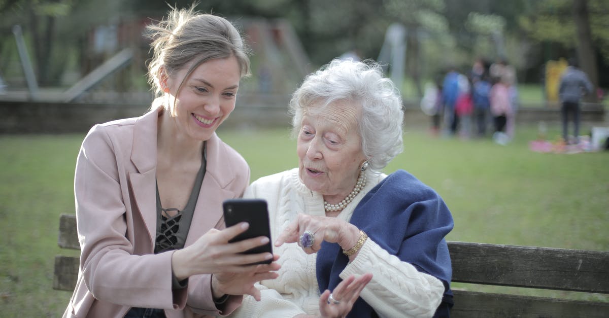 Using mobile internet with a Elephone P7000 in the USA - Delighted female relatives sitting together on wooden bench in park and browsing mobile phone while learning using