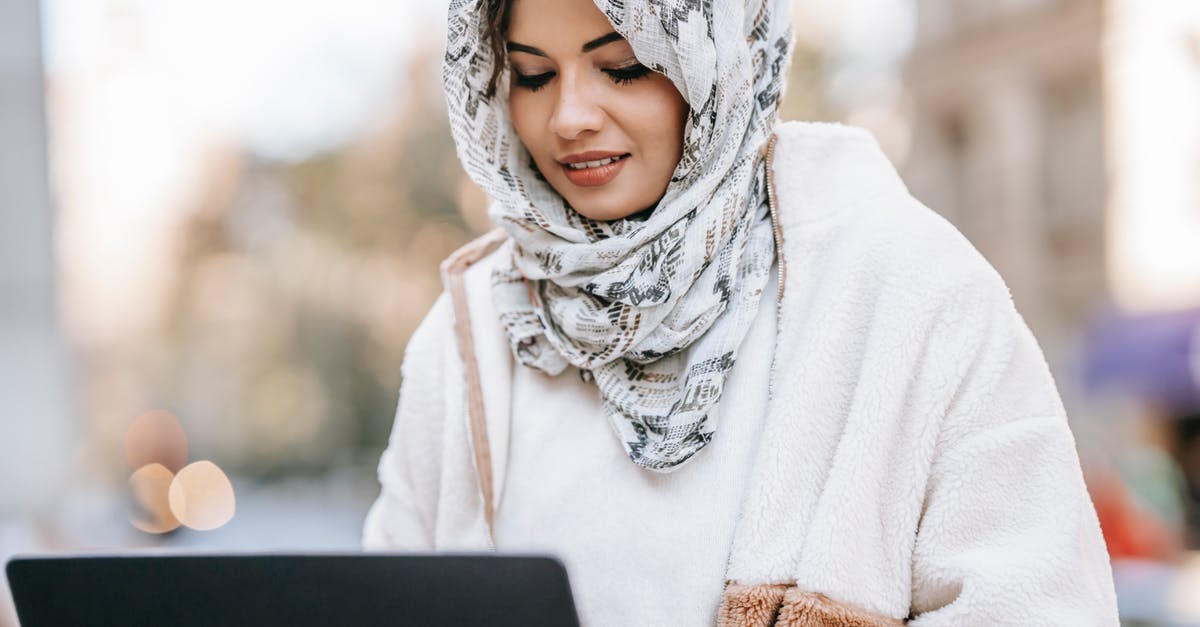 Using Modern Standard Arabic in Arabic-speaking countries - Crop concentrated young ethnic woman in stylish outfit and elegant hijab sitting in street cafe and working remotely on laptop