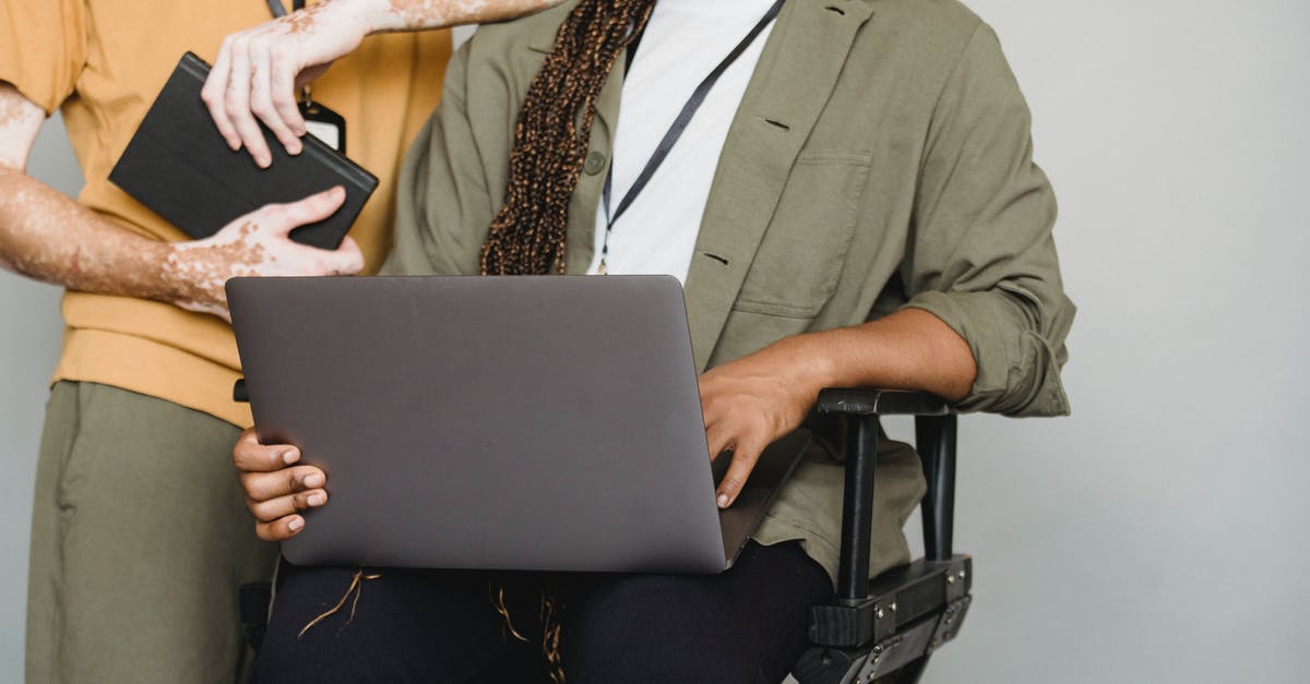 Using my State employee ID in Vegas - Unrecognizable African American male with Afro braids typing on computer while sitting on gray background near colleague with vitiligo and notepad