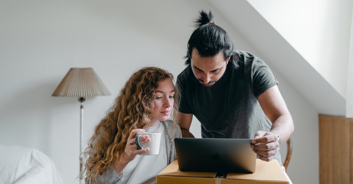 Using parent's property and will as evidence of assets - Concentrated young couple in casual outfit browsing netbook and packing stuff into carton boxes and suitcases to move out