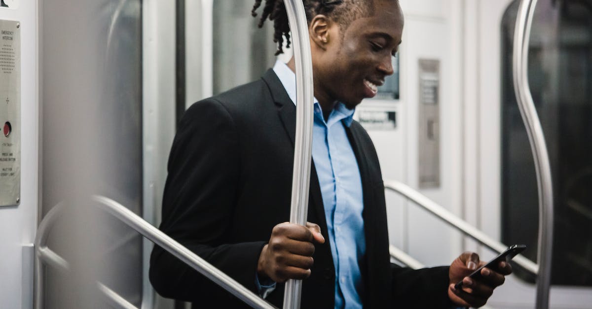 Using public transport in Vancouver: What's my cheapest option? - Cheerful black man surfing net on mobile on subway train