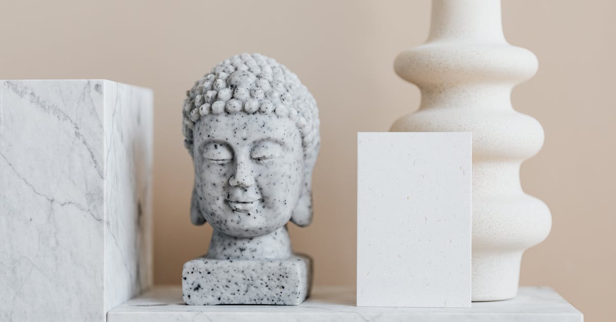 Using Revolut card in Thailand - Granite bust of Buddha placed near white ceramic vase of creative geometric shape and blank card on white marble shelf against beige wall