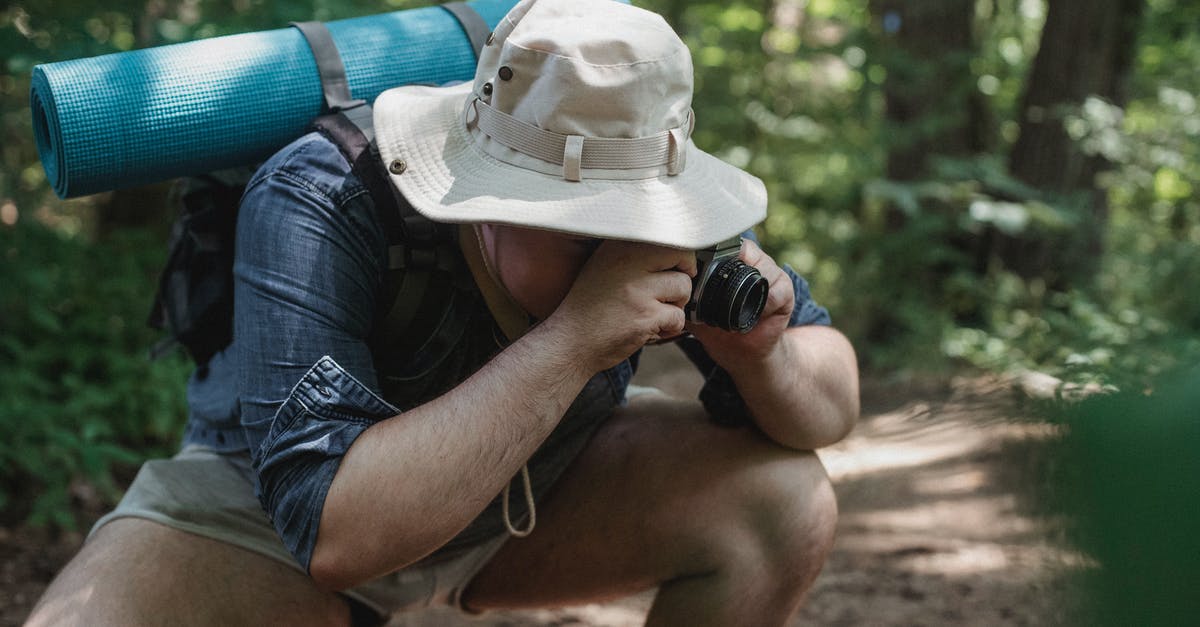 Using squat toilets with arthritic knees - Unrecognizable male tourist with hiking equipment squatting on path while taking photo on camera in summer woods