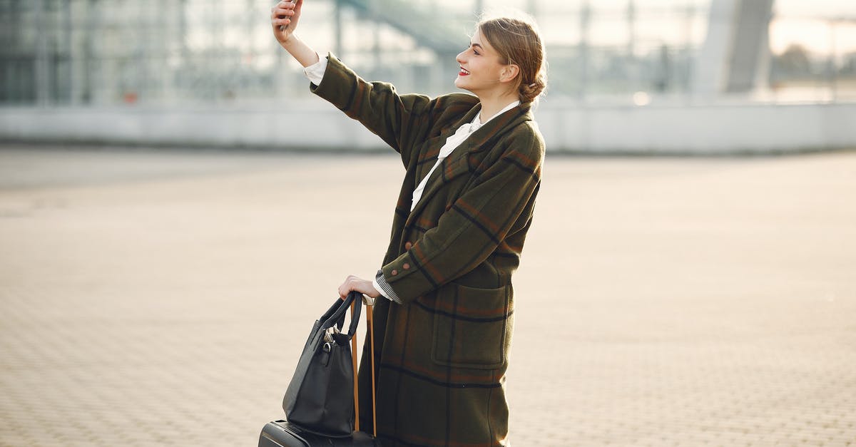 Using Terminal C at Berlin-Schönefeld with checked bags - Stylish young woman with luggage taking selfie outside modern glass building