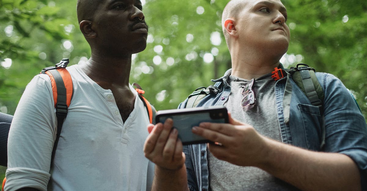 Using the directions setup on a "My Map" using Google Maps - Low angle of focused multiethnic male tourists exploring nature and checking route on mobile phone