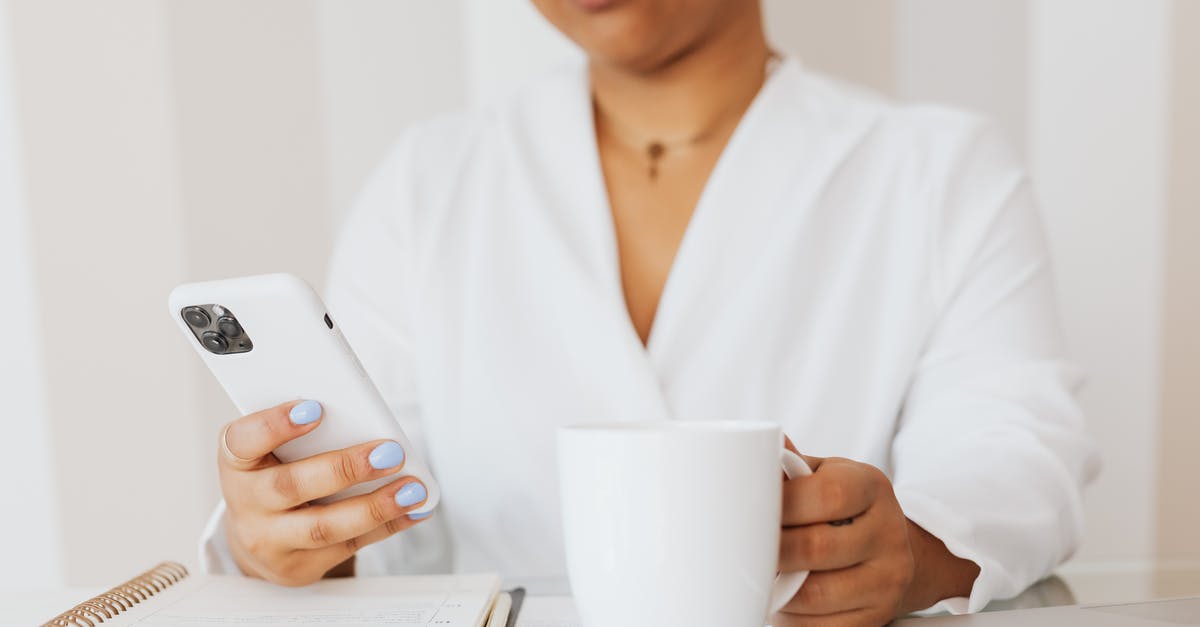 Using US iPhone 6 in Europe - Person in White Top Holding White Ceramic Mug while Using Cellphone