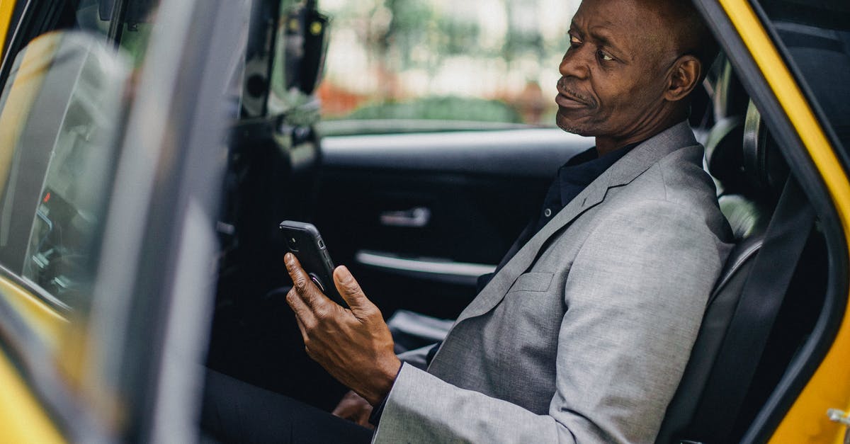 Using USD dollars in taxi in Canada - Contemplative black businessman using smartphone in taxi