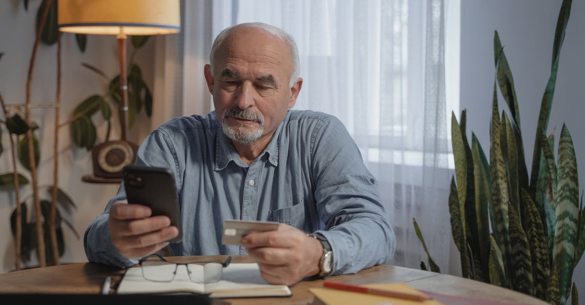 Uzbekistan ATMs and Mastercard - An Elderly Man Using His Mobile Phone while Holding a Credit Card