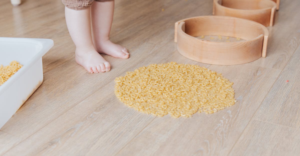 Vancouver YVR getting to quarantine with toddler - Crop faceless toddler standing barefoot on floor and playing with round wooden shapes of different size and pasta developing fine motor skills at home