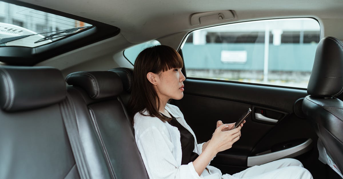 Visa application for a multidestination trip - Side view of focused young Asian female wearing casual white clothes and using modern smartphone while riding at car backseat