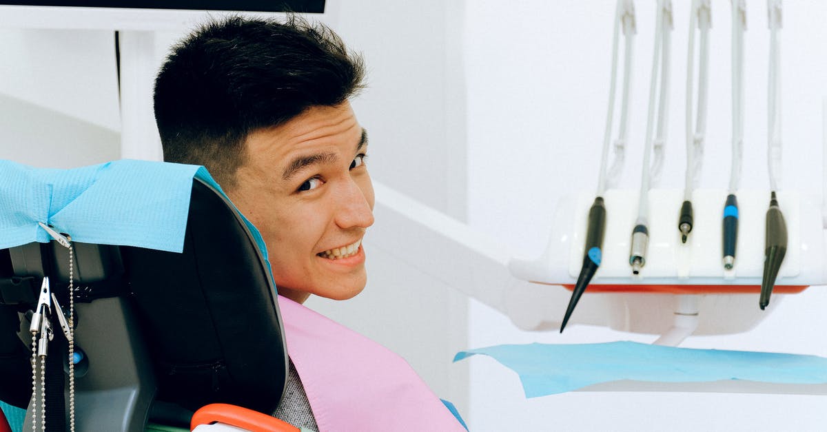 Visa needed to visit friends in London - Back view of smiling ethnic man sitting in chair of dentist while preparing for treatment in modern clinic and looking over shoulder at camera