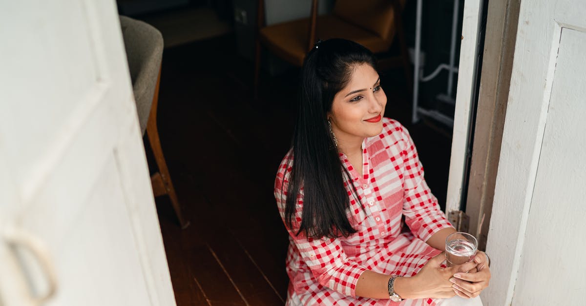 Visa queries from an Indian planning a Machu Picchu, Peru vacation - From above of young Indian lady in casual outfit sitting on floor in doorway with glass of water looking away thoughtfully