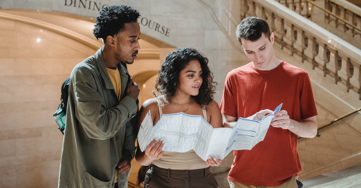 Visa required for a 1 week holiday/conference in NYC - Focused young man pointing at map while searching for route with multiracial friends in Grand Central Terminal during trip in New York