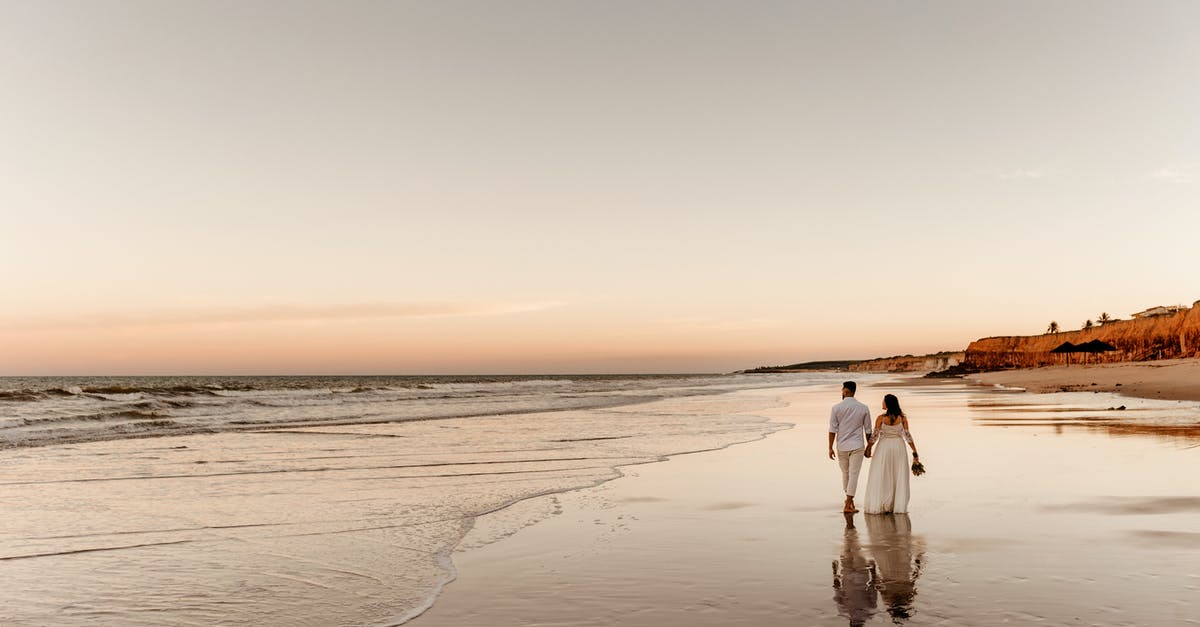 Visa rules regarding travel back to the UK with wife I married abroad - Back view of barefoot groom holding hand of bride in white dress and walking together on sandy coast