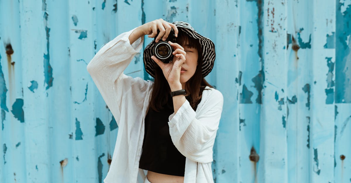 Visa-free countries using US Refugee Travel Document? [closed] - Asian female tourist in striped hat and casual clothes taking photo on professional photo camera while standing with closed eyes near blue ribbed wall with spots on surface