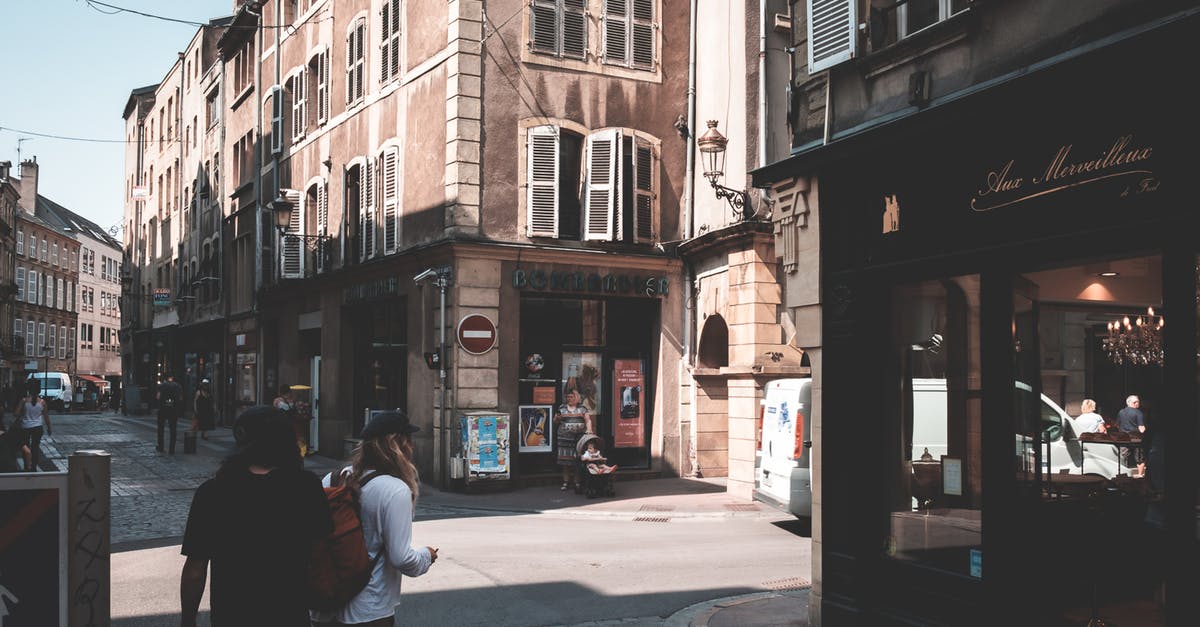 Visa-free visit and re-entry to the UK - Back view of anonymous travelers with backpack strolling on paved walkway between aged buildings with stores on street in shadow