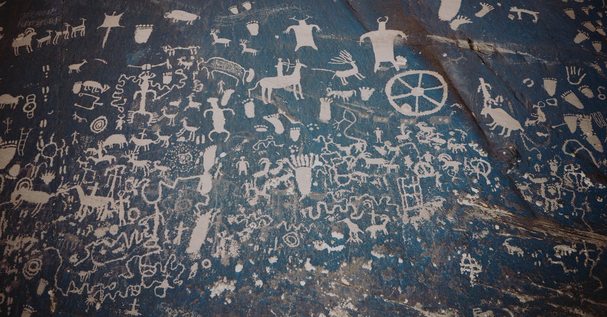 Visiting a National Park in the United States - Newspaper rock with ancient symbols and petroglyphs with white paint on shabby stone blue wall with uneven surface in national park