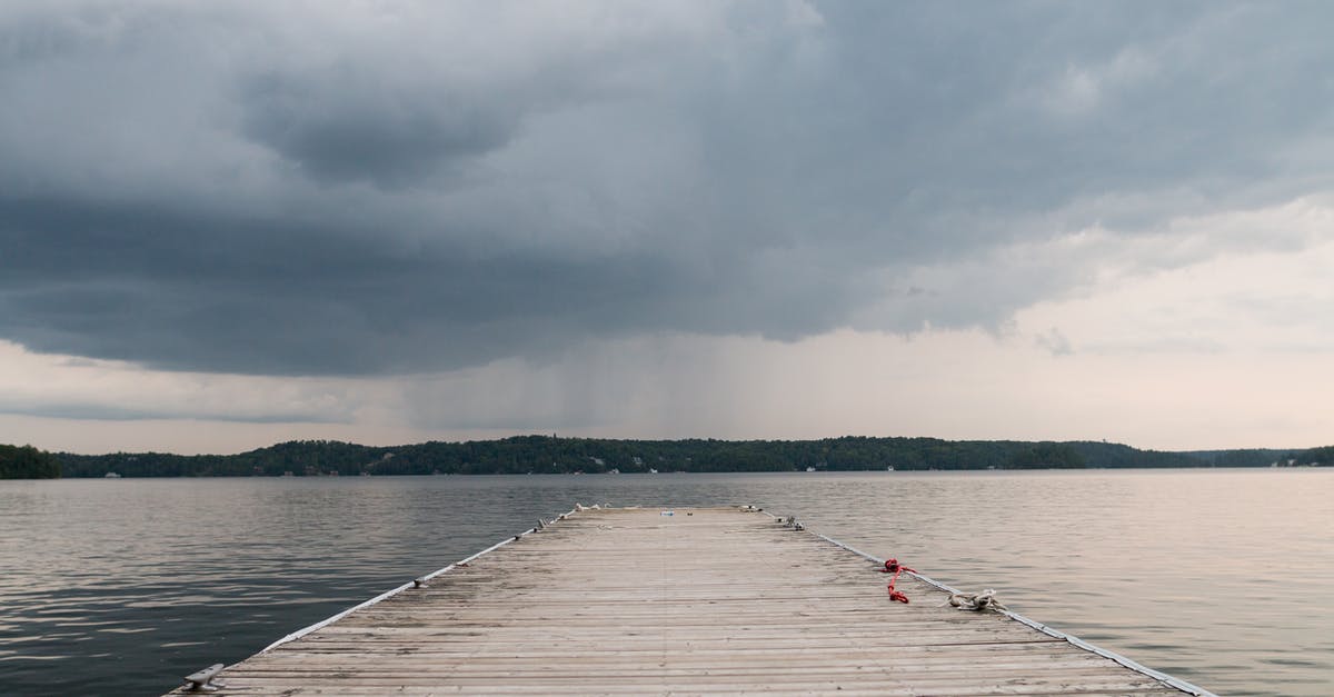 Visiting Canada by land and back - Long berth from wooden boards leading to deep water place against terrain covered with trees and houses under cloudy sky with coming rain