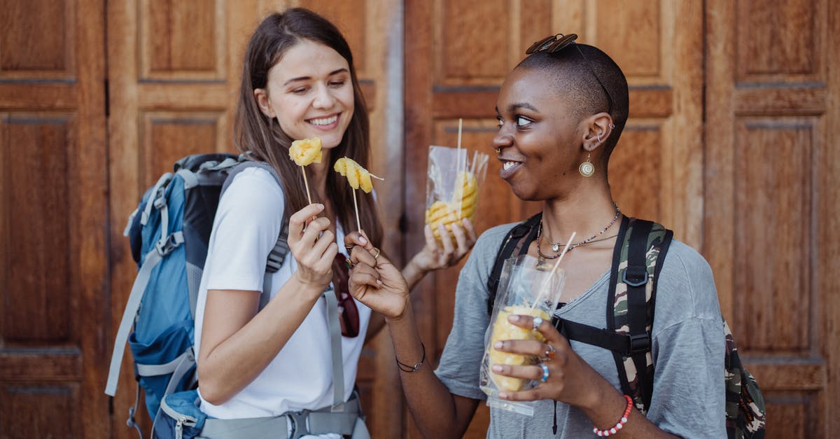 Visiting friends while in transit - Women Travelers Visiting City with Backpacks Eating Pineapple