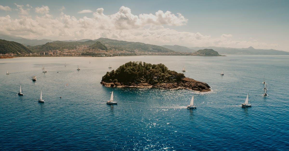 Visiting islands around Cuba - Picturesque seascape of sailboats floating around little island in blue rippling water near hilly coast under cloudy blue sky