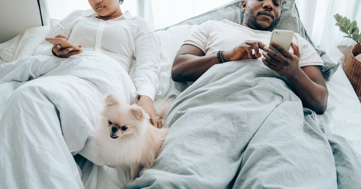 Visiting my spouse in UK [closed] - Crop pensive young couple lying in bed and using smartphone