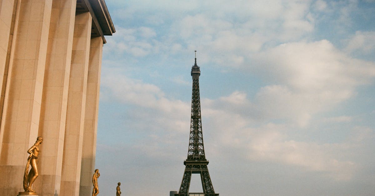 Visiting the Eiffel Tower -- going early to avoid queue - From below of observation tower and aged building exterior with sculptures under cloudy sky in Paris France