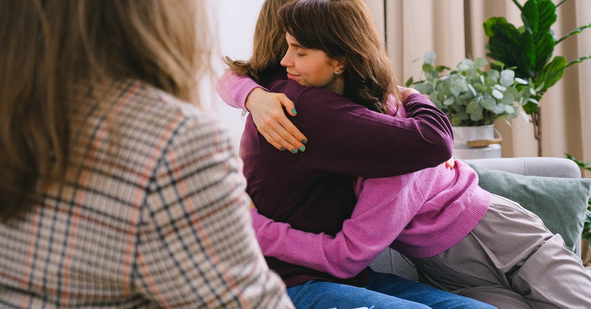 Visiting the UK as unmarried couple - Side view of couple sitting on sofa and embracing during session with psychologist in light room in daytime