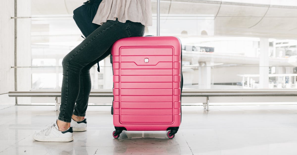 Waiting before passport control in Düsseldorf airport - Woman In White Top And Denim Jeans Sitting  On Red Luggage Bag