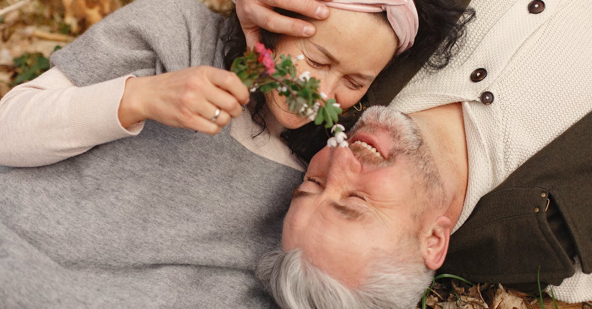 Walk to Sakuranoyama Park from Narita Airport - From above of cheerful senior wife wearing wide scarf and headband with flower bouquet in hand and happy elderly gray haired husband in warm clothes lying on ground with fallen leaves in park with closed eyes