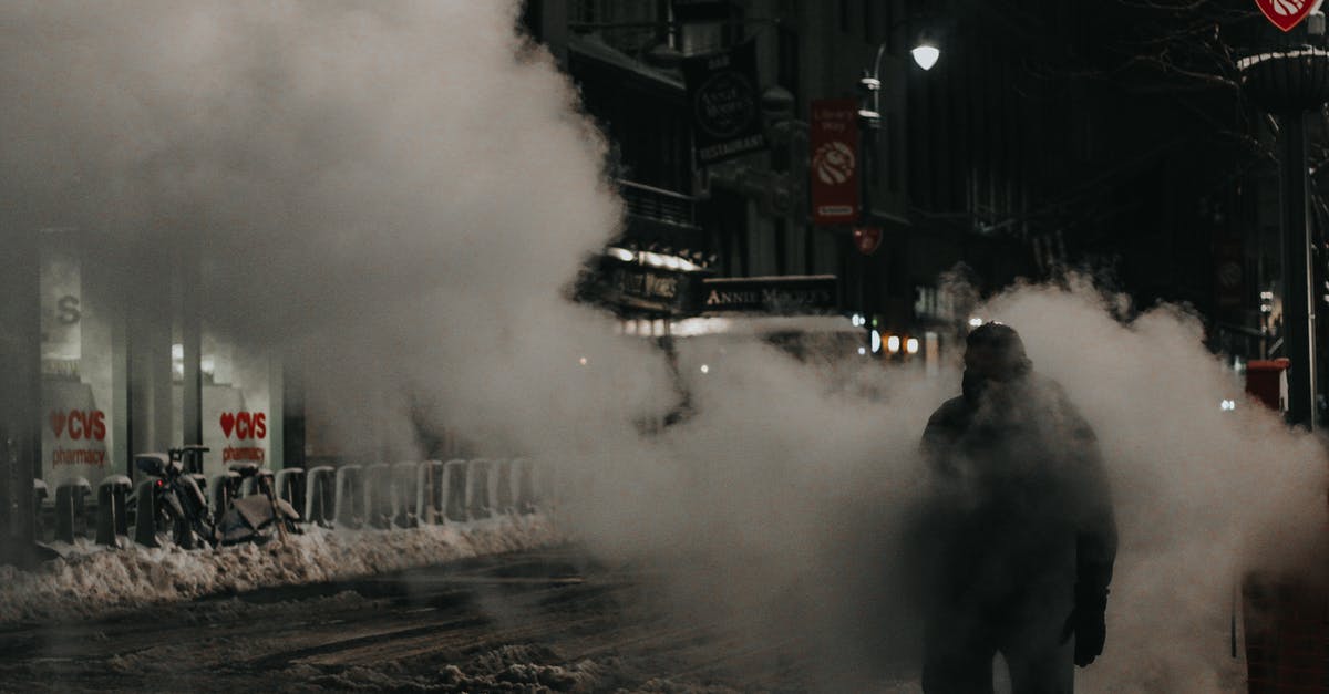 Warm weather options in continental USA in December-January - Anonymous person in warm wear walking through street steam in modern NYC district in winter evening