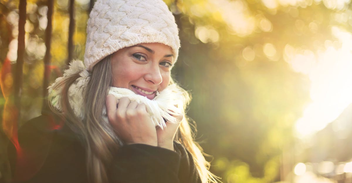 Warm weather options in SE Asia (near Shanghai) in the winter - Young content female wearing warm hat and scarf standing in city garden and enjoying weekend while smiling and looking at camera