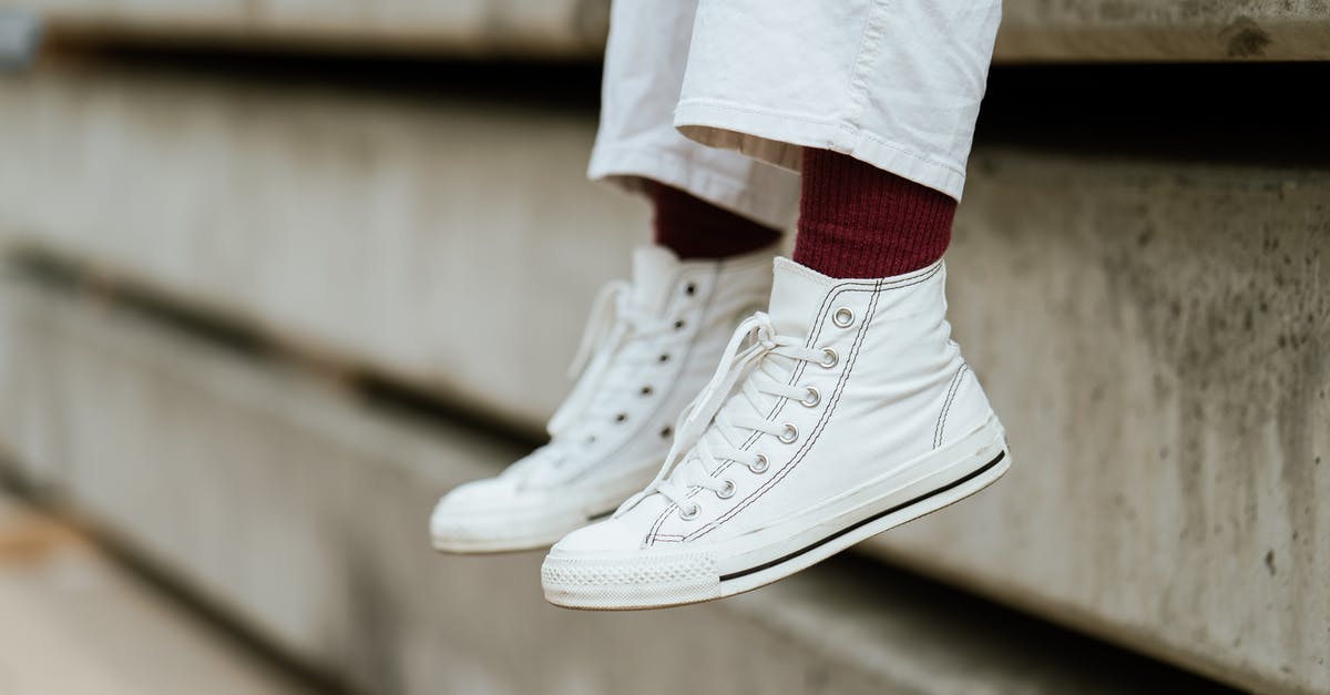 Waterproof shoes or (more comfortable) trainers for walking a lot in Paris in October? [closed] - Crop unrecognizable person in stylish sneakers sitting on concrete beam