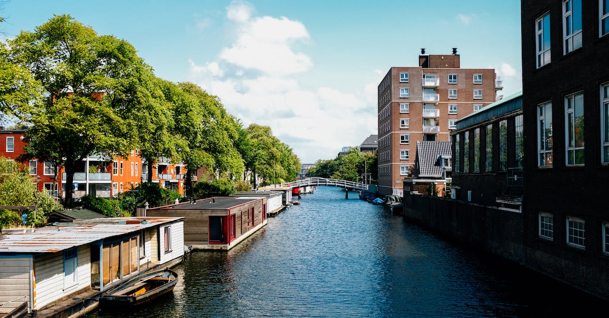 What's a cheap ski location to reach from Amsterdam (Netherlands)? [closed] - Picturesque channel in Amsterdam with traditional houseboats near modern buildings in city outskirts against blue sky