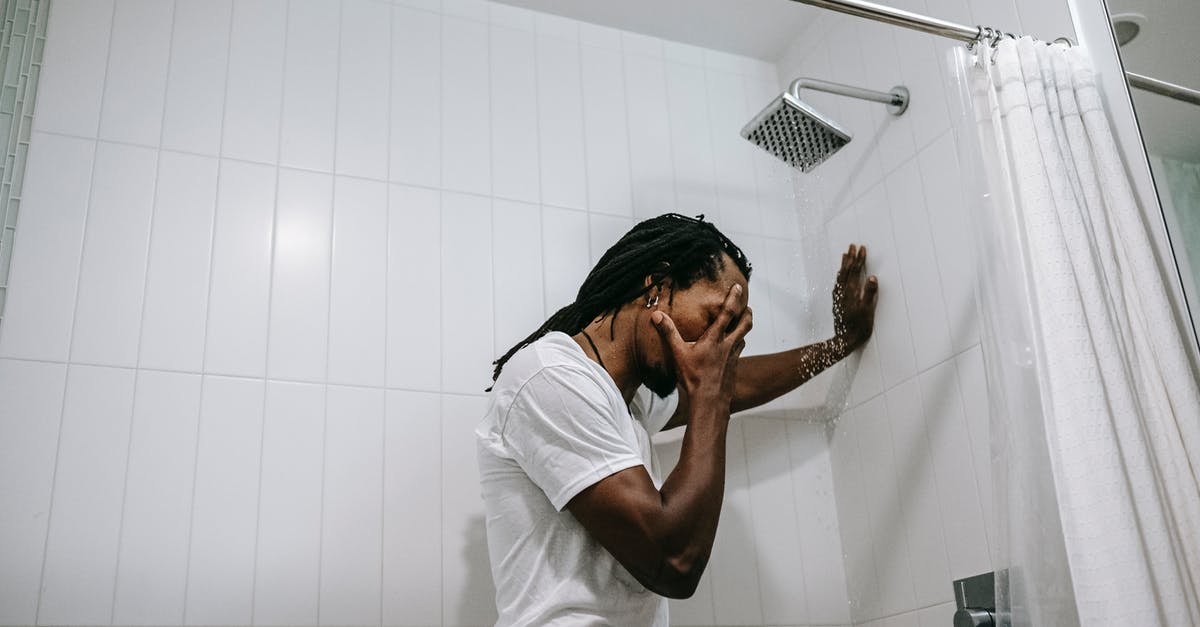 What's the use for this shower drain cover? - Side view depressed preoccupied African American male in white shirt covering face with hand in anxiety in bathroom