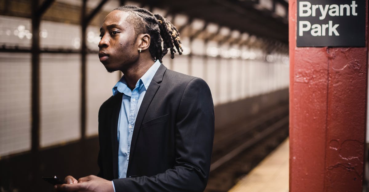 What's with NYC hotel prices in late March? - Young worried African American male commuter in formal suit with smartphone in hands waiting for train at New York subway station