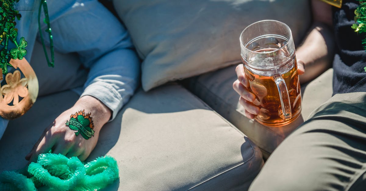 What airlines offer complimentary alcohol from Ireland to the U.S.? - From above of crop unrecognizable man drinking glass of beer while relaxing on cozy couch with male friend with clover tattoo on hand during celebration of St Patricks Day