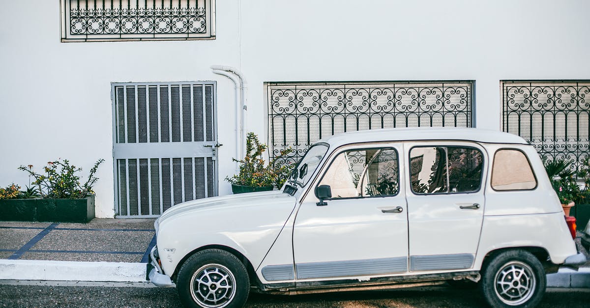 What are Samoan roadside stands selling in white styrofoam cups? - Old vintage white automobile parked on asphalt city street outside white house with bars on windows and lawn if front on sunny day