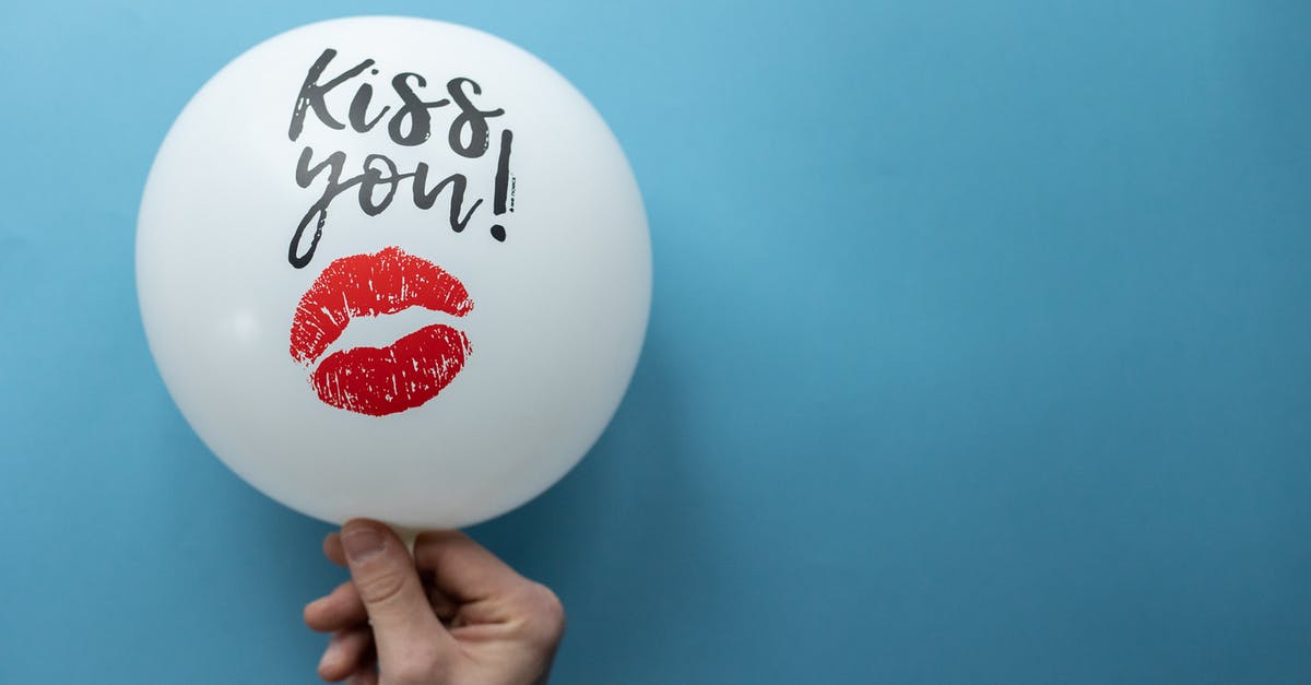 What are some practical hand-out gifts you can take with you when travelling? - Unrecognizable person demonstrating white balloon with Kiss You inscription and kiss mark on blue background in studio during holiday celebration