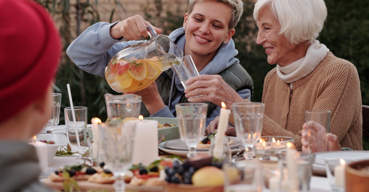 What are the candles outside in Denmark about? - Positive lady pouring drink into glass for elderly woman while having dinner with family on terrace