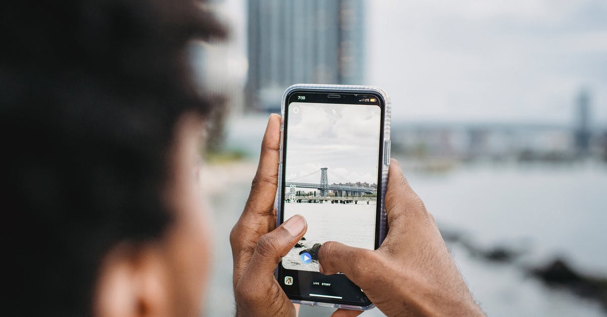 What coast or river-adjacent city is in this photo? - Black man taking photo of bridge over river