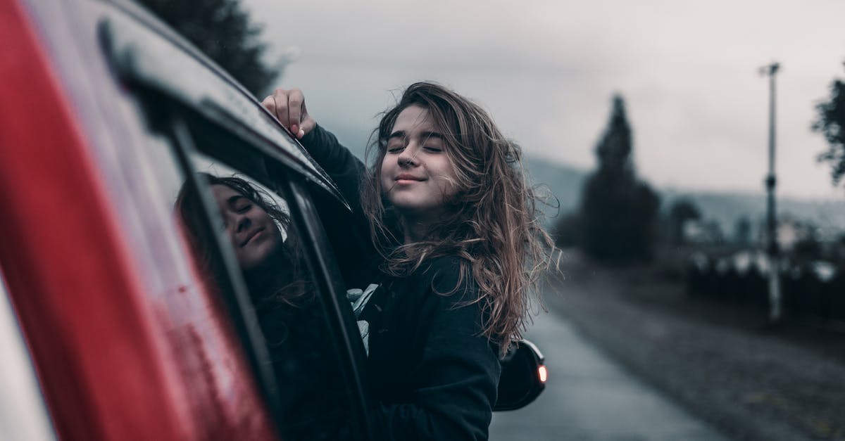 What dangers should I keep in mind while driving in the Dominican Republic? [closed] - Side view of young dreamy ethnic female with closed eyes leaning out automobile window driving on asphalt road near trees and mountains under sky in countryside