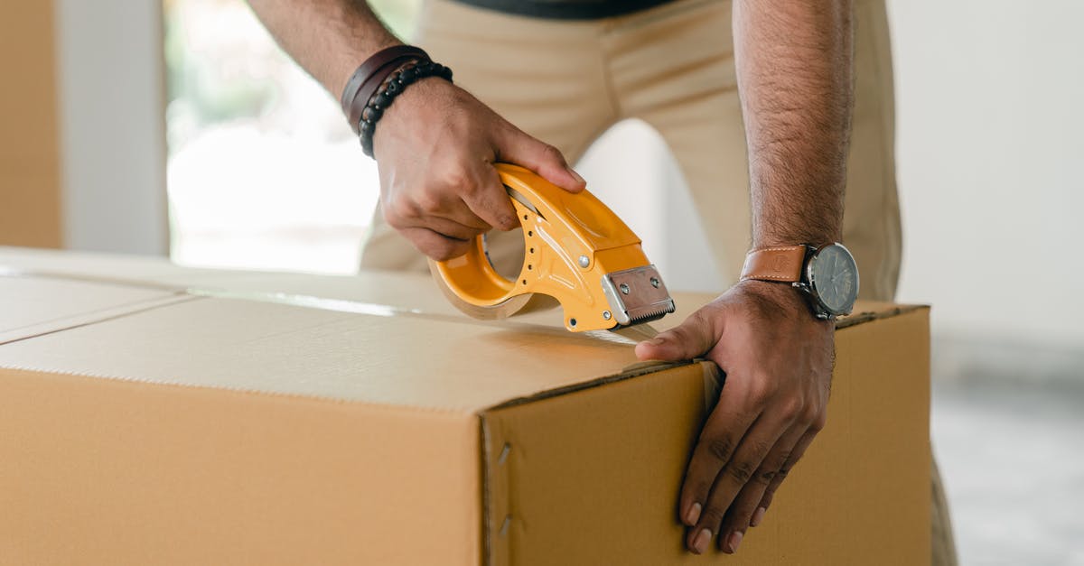What do I need to know or do in order to rent a car in Spain? - Crop faceless young male with wristwatch using adhesive tape while preparing cardboard box for transportation