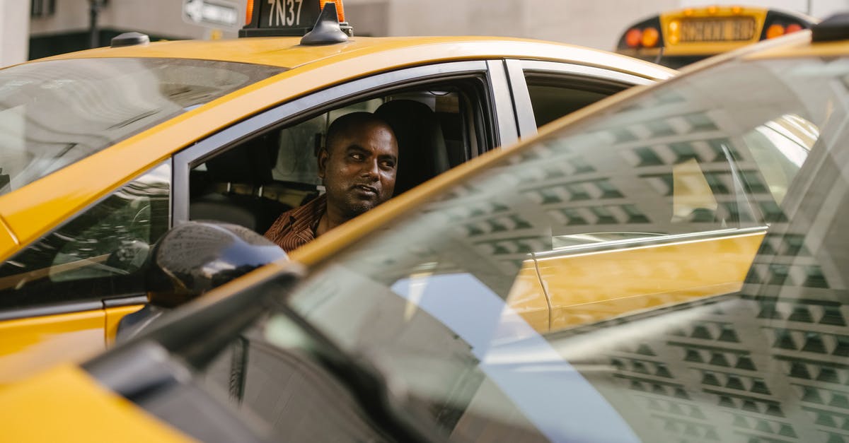 What do these numbers (1, 2, 3) on taxi roofs mean? - Adult ethnic male taxi driver sitting in contemporary auto and looking away near similar vehicle reflecting urban building