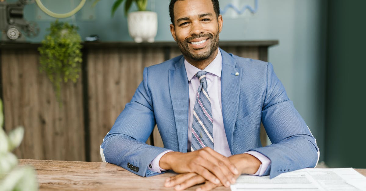 What documents should I submit after refusal of a visit visa? - Smiling Man in Blue Suit Sitting by the Table