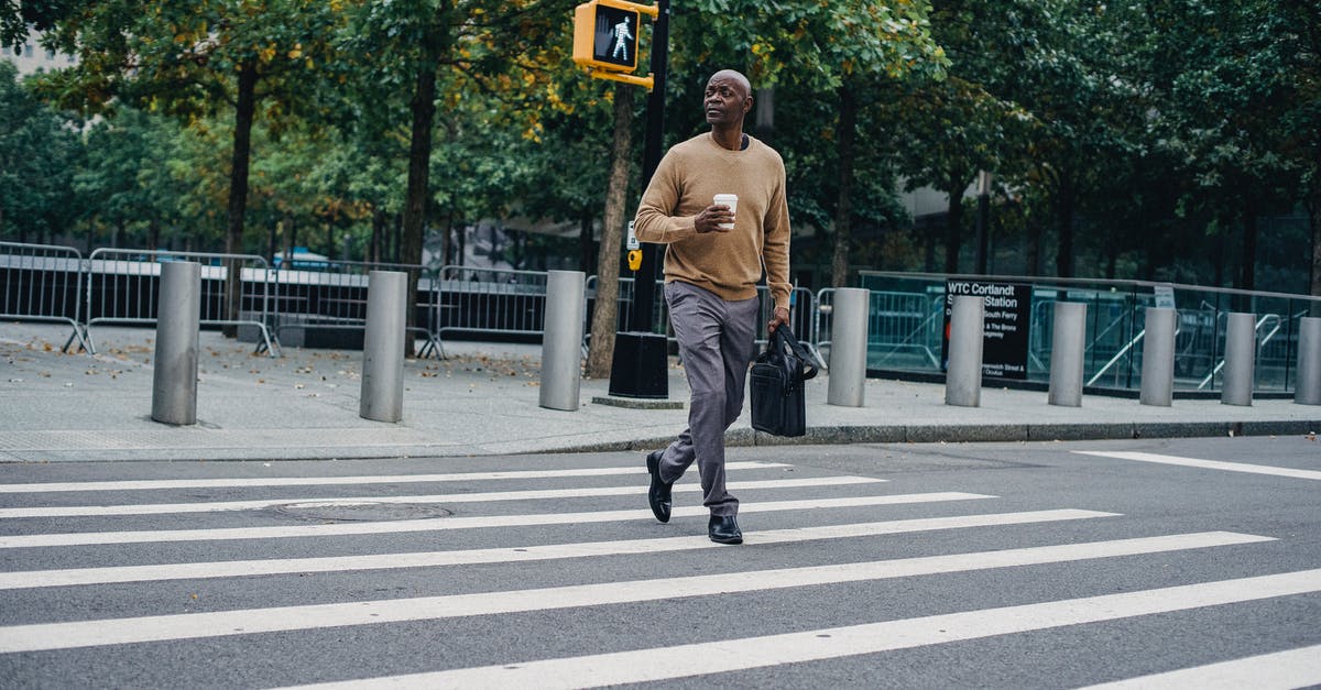 What does amber - green traffic light mean in South Korea? - Full body of African American male walking on pedestrian crossing on asphalt road with cup of hot drink and briefcase