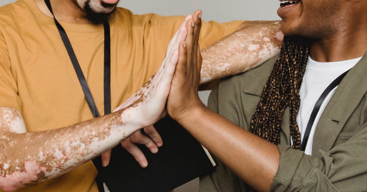 What does "in good health" mean with respect to Canadian entry? - Crop smiling African American male with vitiligo skin giving high five to colleague in studio