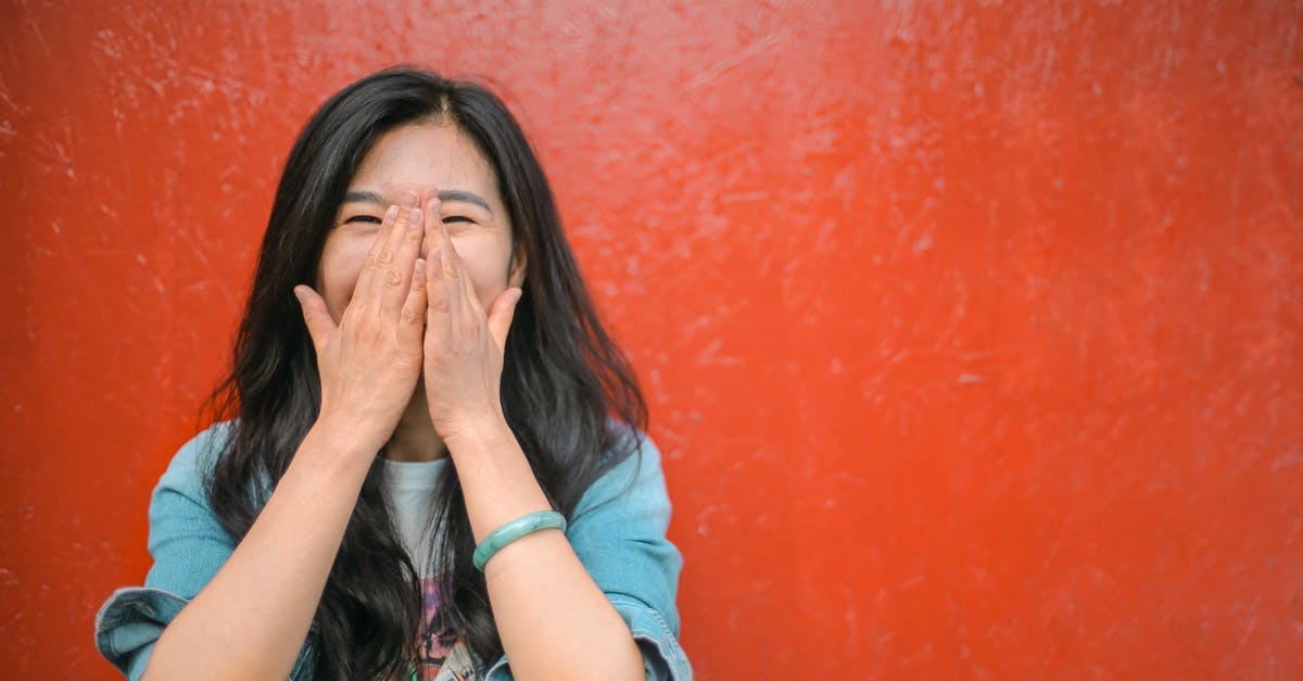 What does red painted bus stop mean in UK? - Young overjoyed Asian female in casual outfit covering face with hands and laughing while standing against vibrant orange wall