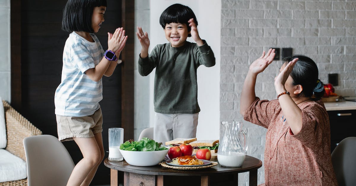 What game can I eat in South Africa? - Joyful Asian grandmother and grandchildren wearing casual clothes having lunch and playing patty cake game in modern light living room