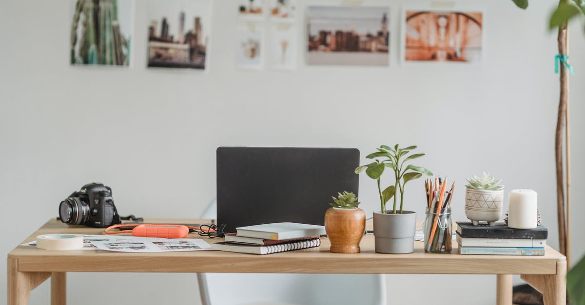 What happens if a UK digital passport photo is rejected? - Wooden table with modern netbook and photo camera placed near printed photos with small decorative flowerpots at wall with pictures