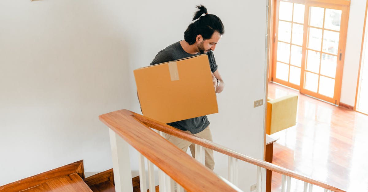 What happens to items removed from luggage? - From above of full length male in casual clothes carrying carton box down stairs while moving personal items to new house